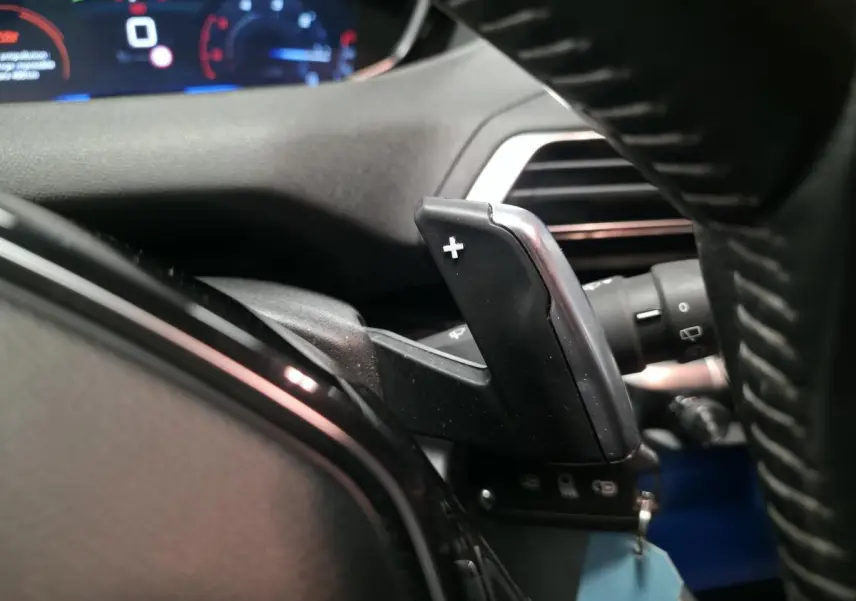 Gros plan sur la palette de changement de vitesse droite du volant d'une Peugeot 5008 gris, tableau de bord en arrière-plan flou.