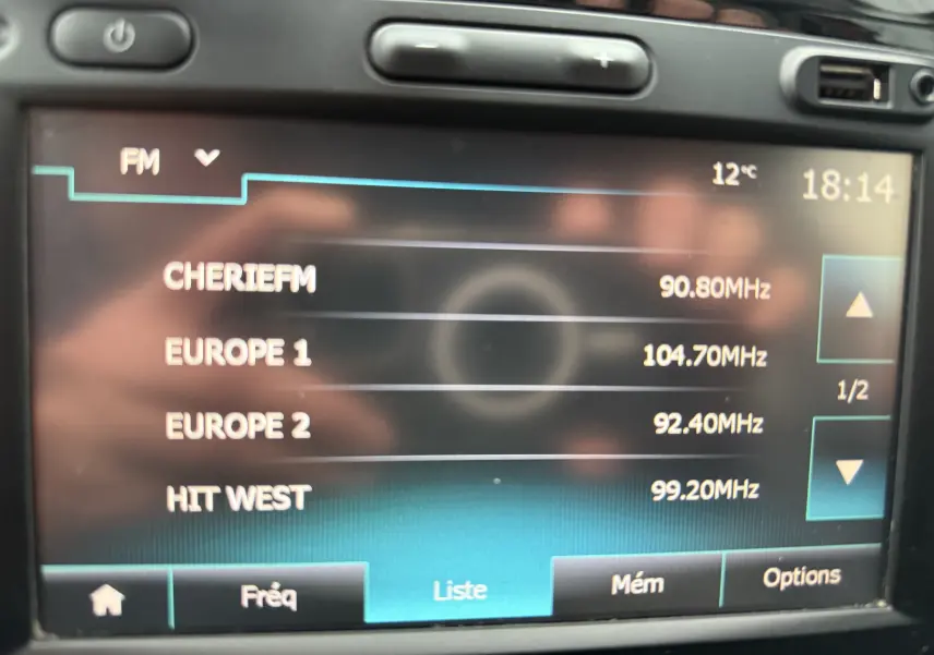 Écran central du système multimédia du Renault Captur rouge, affichant la liste des stations FM avec l'heure et la température.