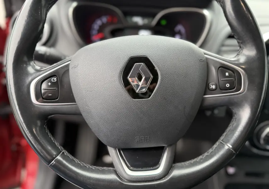Gros plan sur le volant en cuir noir du Renault Captur rouge, avec commandes intégrées et airbag central.
