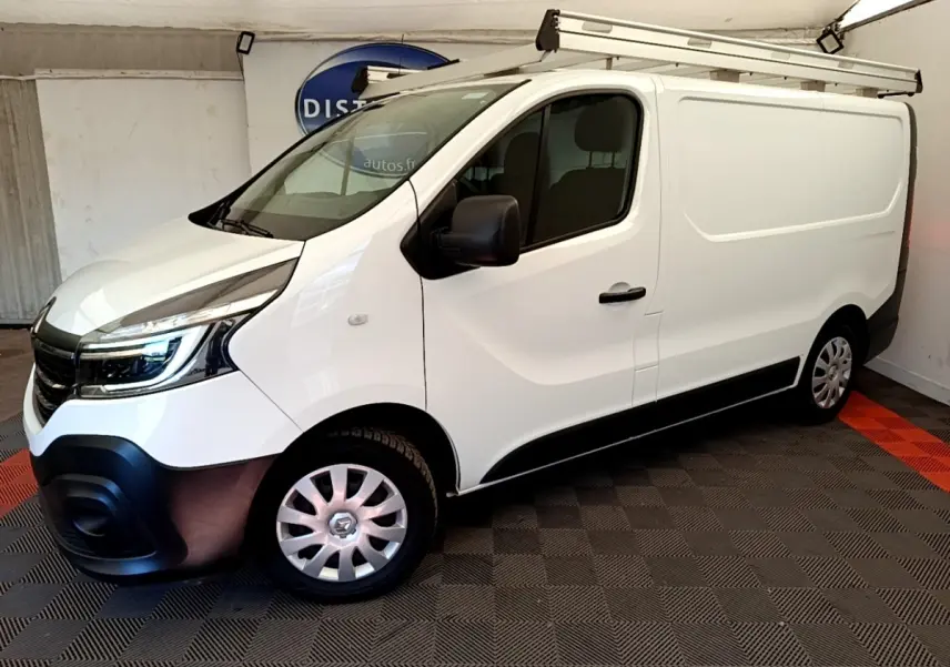 Renault Trafic Fourgon blanc en vue 3/4 avant droit, avec galerie de toit et jantes acier argentées.