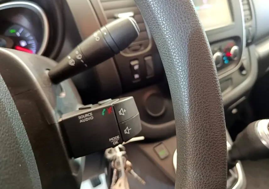 Gros plan sur le volant noir et la commande audio au volant du Renault Trafic Fourgon blanc, version 2021.