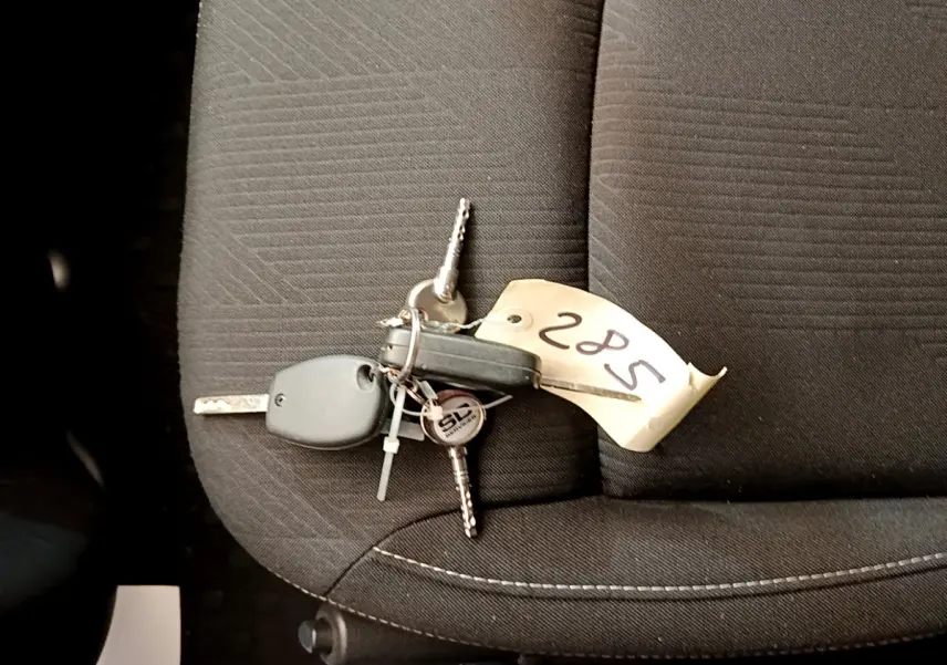 Jeu de clés avec télécommande posé sur un siège avant en tissu gris foncé à coutures blanches du Renault Trafic Fourgon blanc.