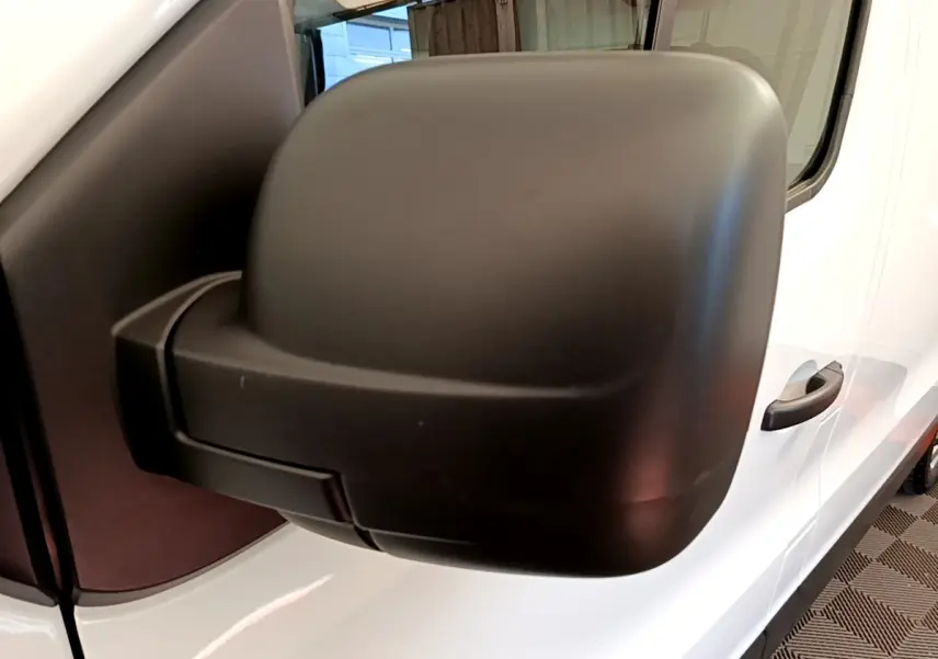 Gros plan sur le rétroviseur noir côté conducteur du Renault Trafic Fourgon blanc, vue latérale droite.