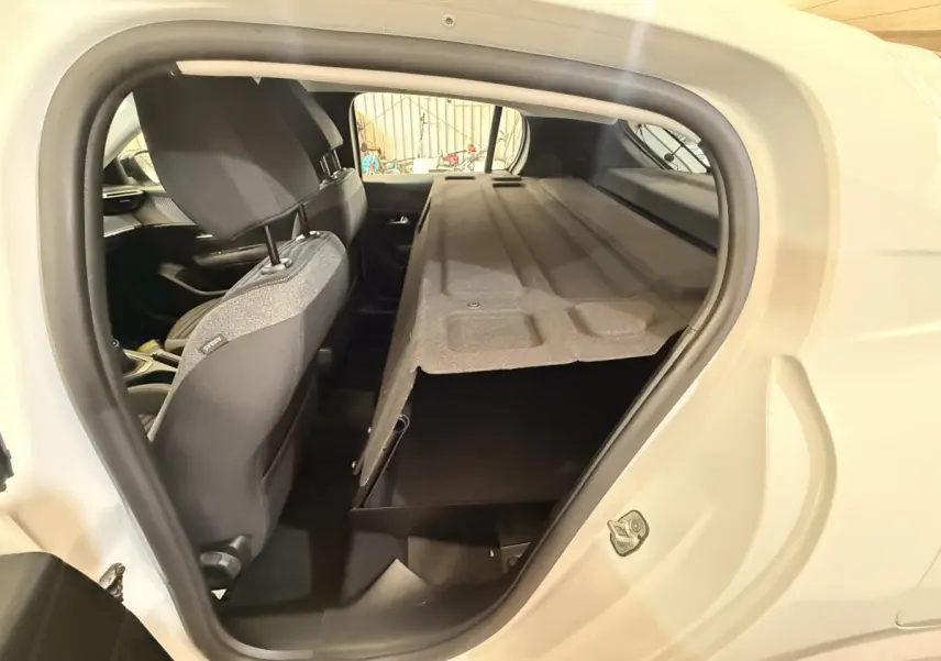 Vue intérieure côté gauche du coffre ouvert d'une Peugeot 208 blanche, avec banquette arrière rabattue.