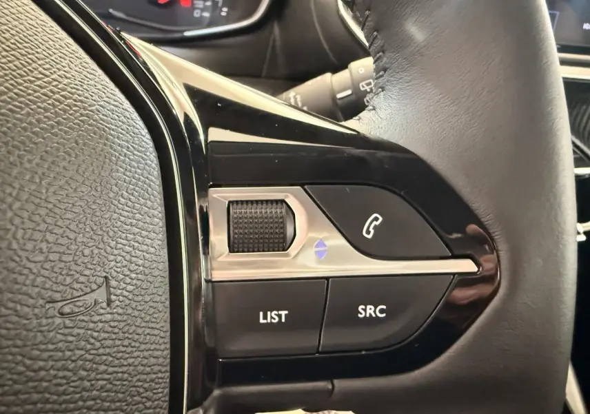Gros plan sur les commandes gauche du volant cuir noir de la Peugeot 208 2025, avec boutons LIST, SRC et téléphone.
