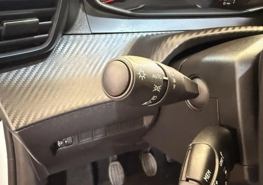 Gros plan sur la commande des phares et du régulateur de vitesse dans l'habitacle noir d'une Peugeot 208 blanche.