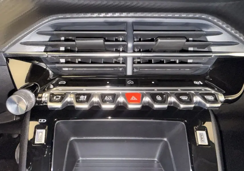 Gros plan sur la console centrale noire de la Peugeot 208 blanche, avec boutons de commande et prises USB visibles.