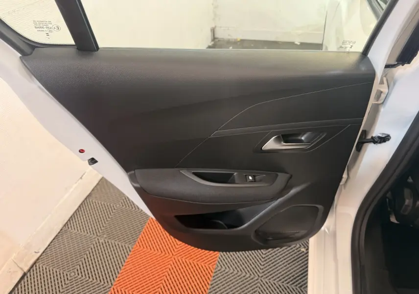 Vue intérieure de la porte arrière droite noire d'une Peugeot 208 blanche 2025, avec poignée et commande de vitre.
