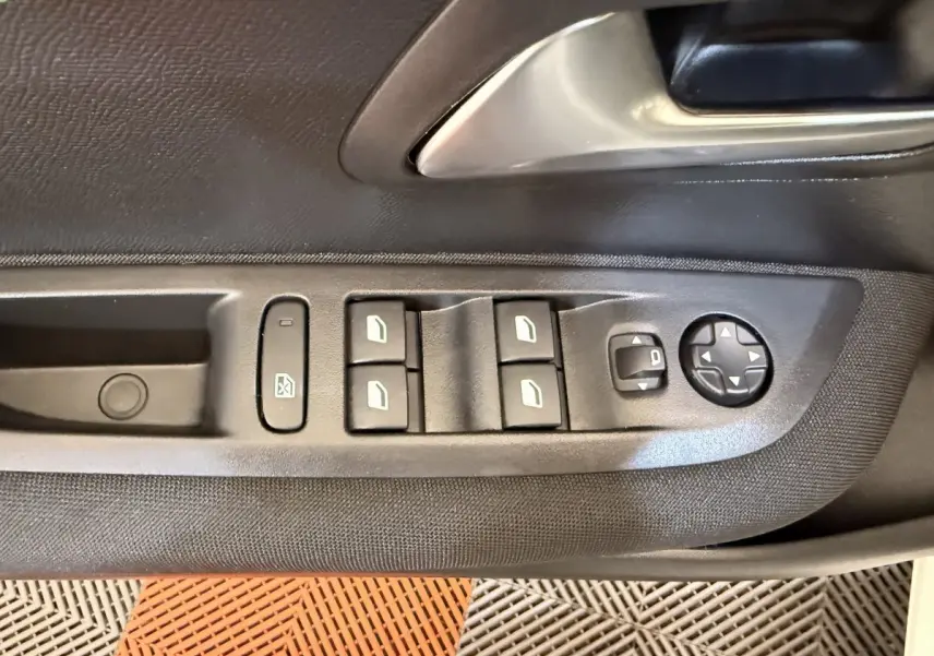 Gros plan sur la commande des vitres et rétroviseurs côté conducteur d'une Peugeot 208 blanche, intérieur noir.