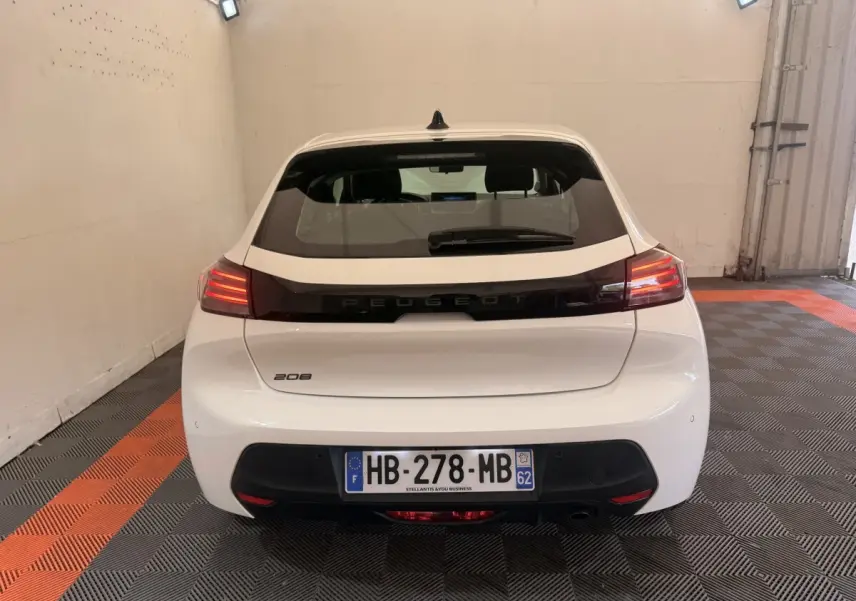 Vue arrière d'une Peugeot 208 blanche 2025 garée en intérieur avec feux arrière allumés et plaque d'immatriculation française.