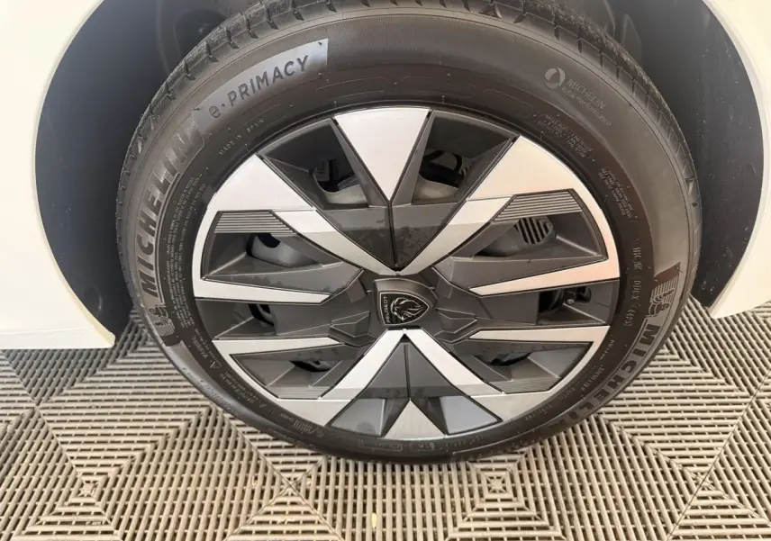 Gros plan sur la roue avant gauche blanche d’une Peugeot 208 2025 avec jante stylisée bicolore et pneu Michelin.