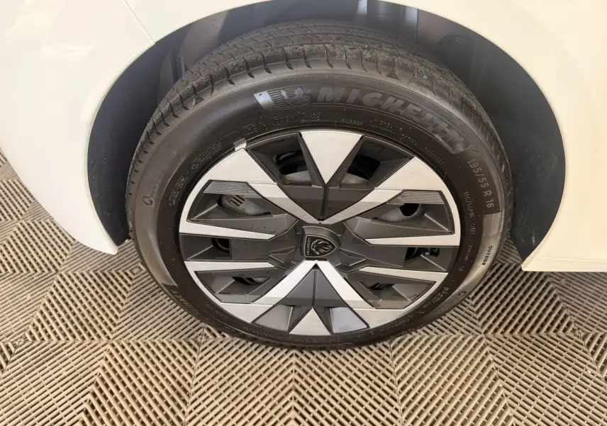 Gros plan sur la roue avant droite blanche d'une Peugeot 208 2025 avec jante au design géométrique noir et argent.