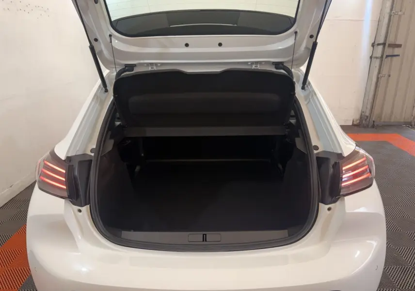 Vue arrière ouverte du coffre d'une Peugeot 208 blanche 2025, avec feux arrière allumés et intérieur de coffre vide.