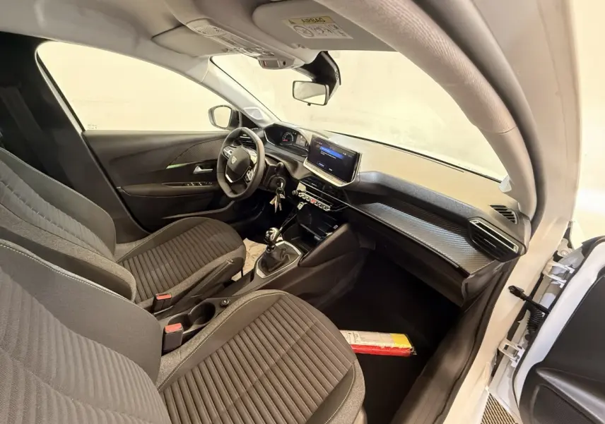 Vue intérieure côté conducteur de la Peugeot 208 blanche 2025, montrant sièges noirs et tableau de bord avec écran tactile.