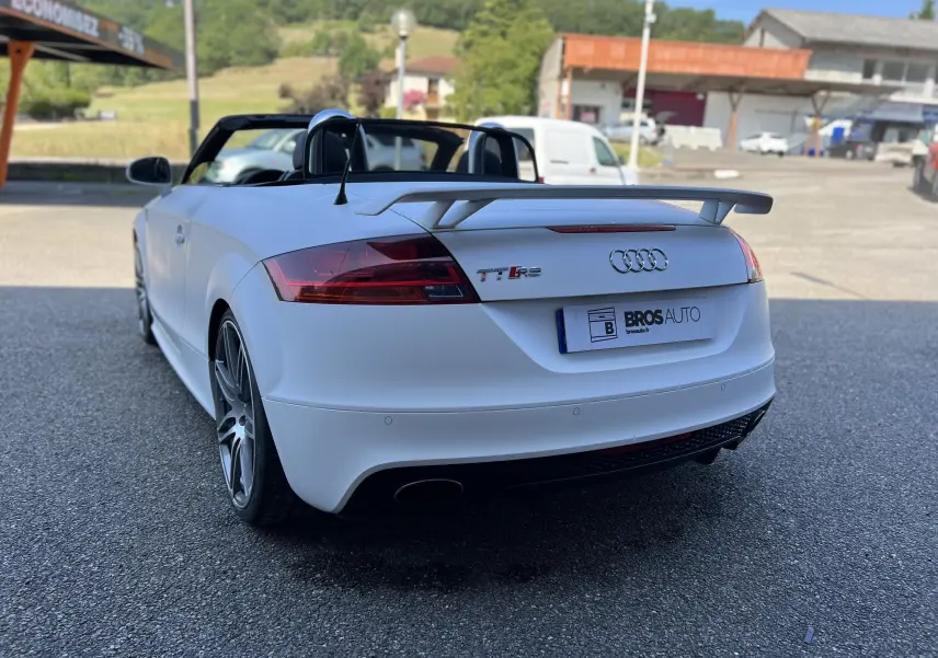 Audi TT RS Roadster blanc vu de l'arrière droit, capote ouverte et aileron arrière distinctif visible.