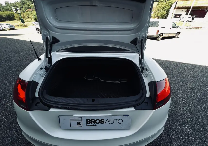 Coffre ouvert vu de l'arrière d'une Audi TT RS Roadster cabriolet blanc avec feux arrière rouges visibles.