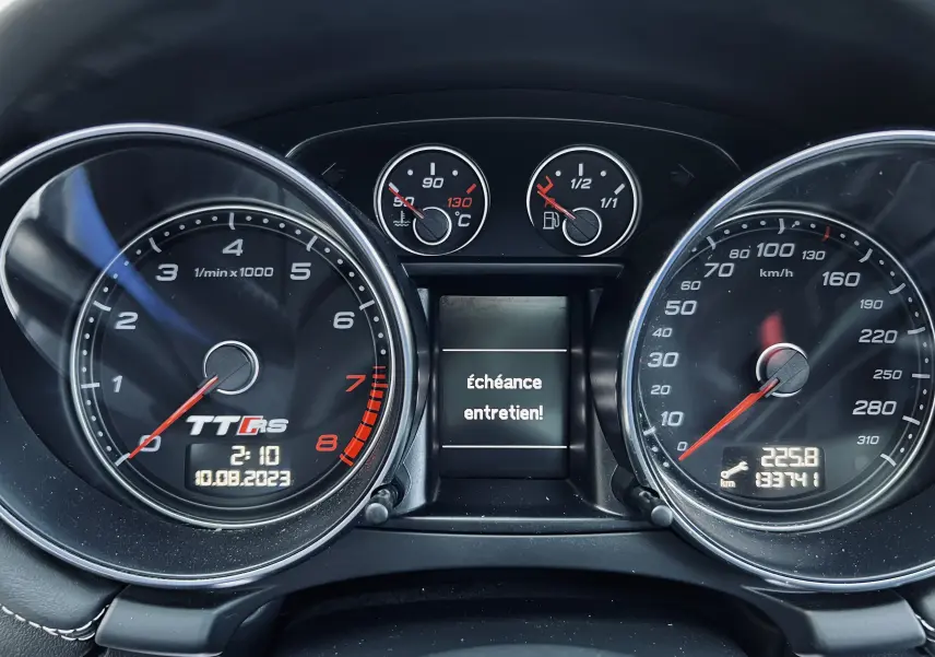 Vue rapprochée du tableau de bord de l'Audi TT RS avec compte-tours, vitesse et message d'entretien affiché.