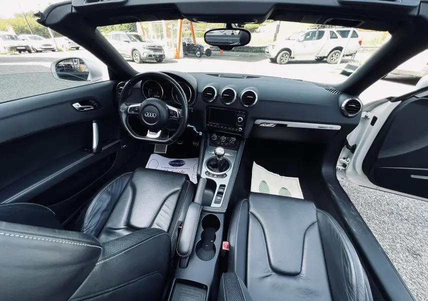 Vue intérieure frontale de l'Audi TT RS Roadster blanc, avec sièges baquet cuir noir et volant multifonction.
