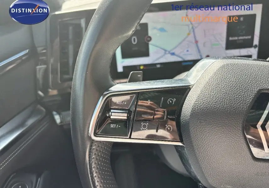 Gros plan sur le volant noir perforé du Renault Austral 2024 avec commandes intégrées et écran de navigation en arrière-plan.