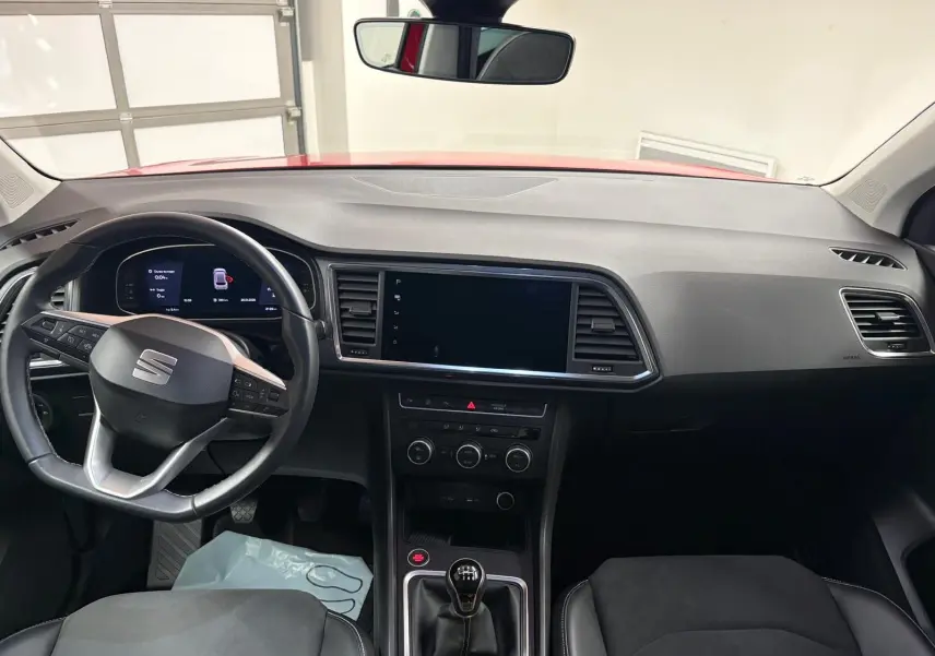 Vue intérieure avant du tableau de bord et volant de la SEAT Ateca 2024 avec boîte manuelle et toit rouge visible par le pare-brise.