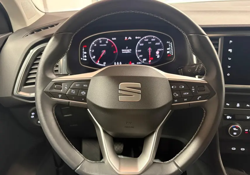 Vue rapprochée du volant noir du SEAT Ateca 2024 avec commandes intégrées et tableau de bord numérique allumé.