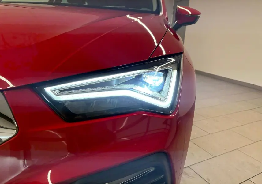 Gros plan sur le phare avant gauche allumé d’un SEAT Ateca 2024 Rouge Velvet avec peinture métallisée.