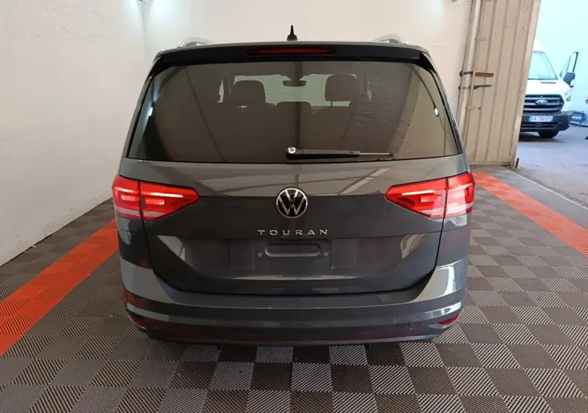 Vue arrière d’un Volkswagen Touran gris clair 2024 avec feux arrière allumés dans un garage.