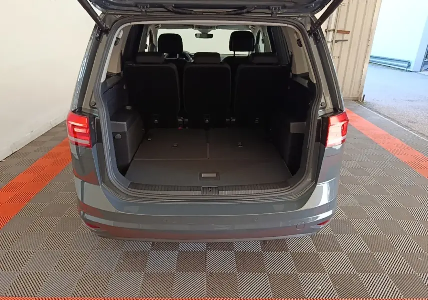 Vue arrière ouverte du Volkswagen Touran gris clair 2024, montrant le coffre spacieux avec sièges rabattus.