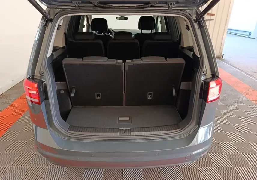 Vue arrière du coffre ouvert d'un Volkswagen Touran gris clair 2024 avec sièges arrière en position verticale.