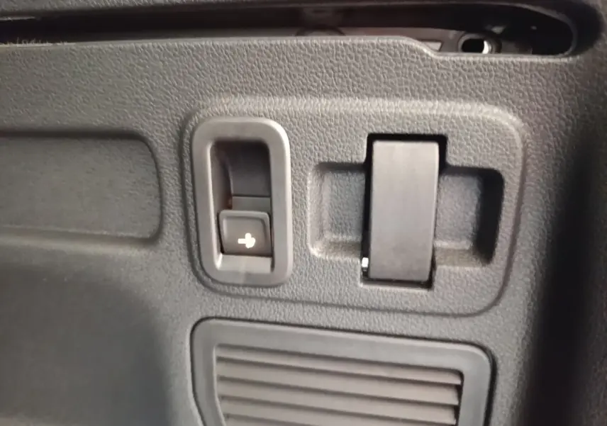 Détail intérieur montrant un bouton de rabattement des sièges dans le coffre du Volkswagen Touran gris clair 2024.