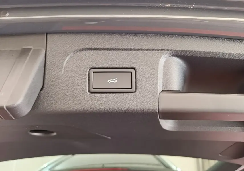 Bouton d'ouverture électrique du coffre sur la partie intérieure du hayon d'un Volkswagen Touran gris clair.