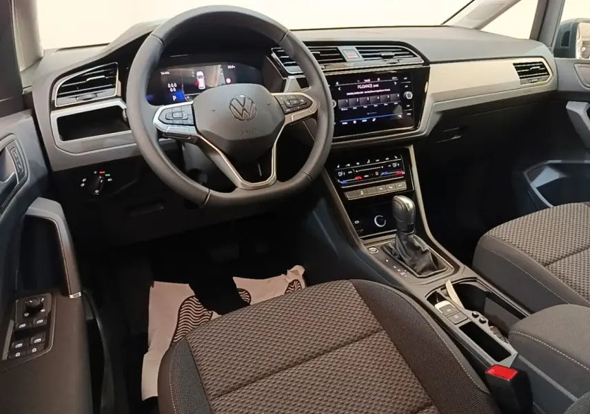 Vue intérieure côté conducteur du Volkswagen Touran 2024, tableau de bord noir avec écran tactile central et volant multifonctions.