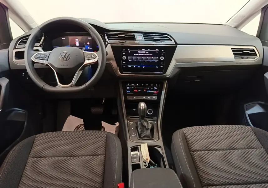Vue intérieure avant du Volkswagen Touran 2024, tableau de bord gris clair avec écran tactile et volant multifonctions cuir.