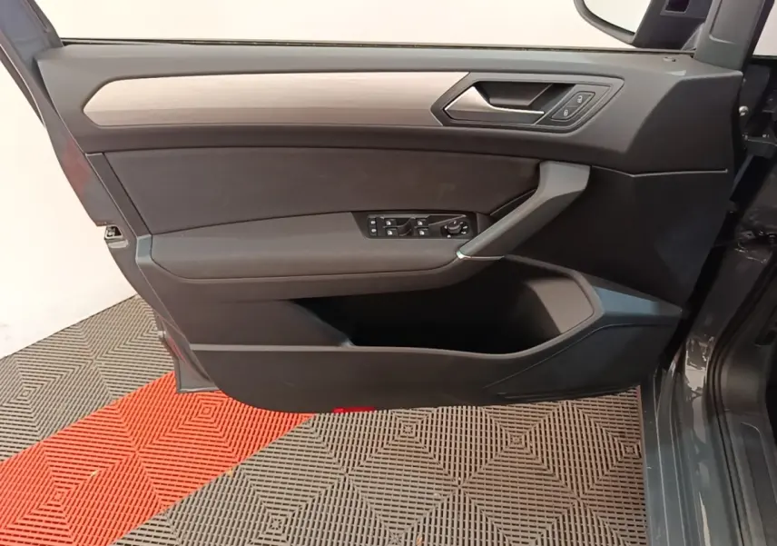 Vue côté gauche de la porte avant gris clair du Volkswagen Touran 2024 avec commandes électriques et insert bois.