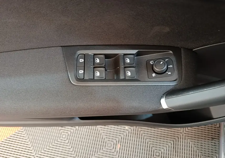 Gros plan sur la commande des vitres et rétroviseurs côté conducteur d’un Volkswagen Touran gris clair 2024.
