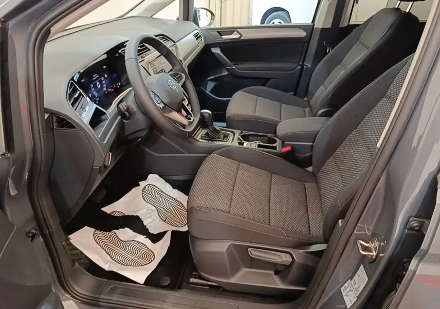 Vue intérieure côté conducteur du Volkswagen Touran gris clair 2024, montrant sièges tissu et tableau de bord digital.