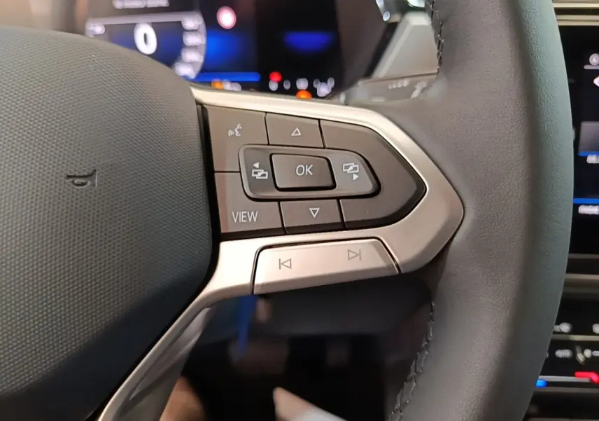 Gros plan sur le volant cuir gris du Volkswagen Touran 2024 avec commandes multifonctions et affichage digital en arrière-plan.