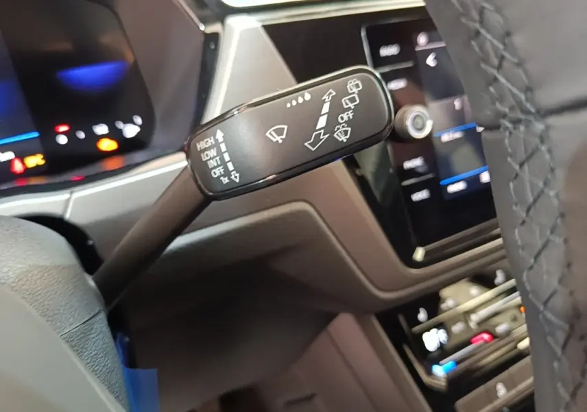 Gros plan sur la commande des essuie-glaces à gauche du volant dans l’habitacle du Volkswagen Touran gris clair 2024.