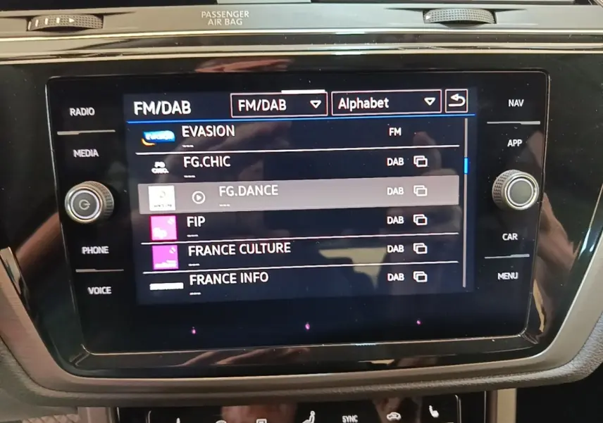 Gros plan sur l'écran tactile central du Volkswagen Touran 2024 affichant les stations radio FM/DAB.