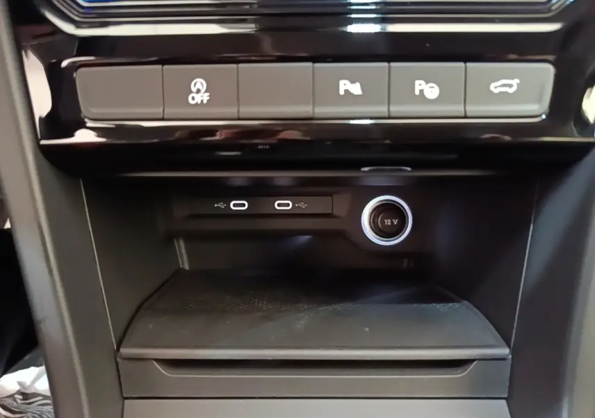 Gros plan sur la console centrale noire du Volkswagen Touran 2024 avec ports USB-C, prise 12V et boutons d’assistance.