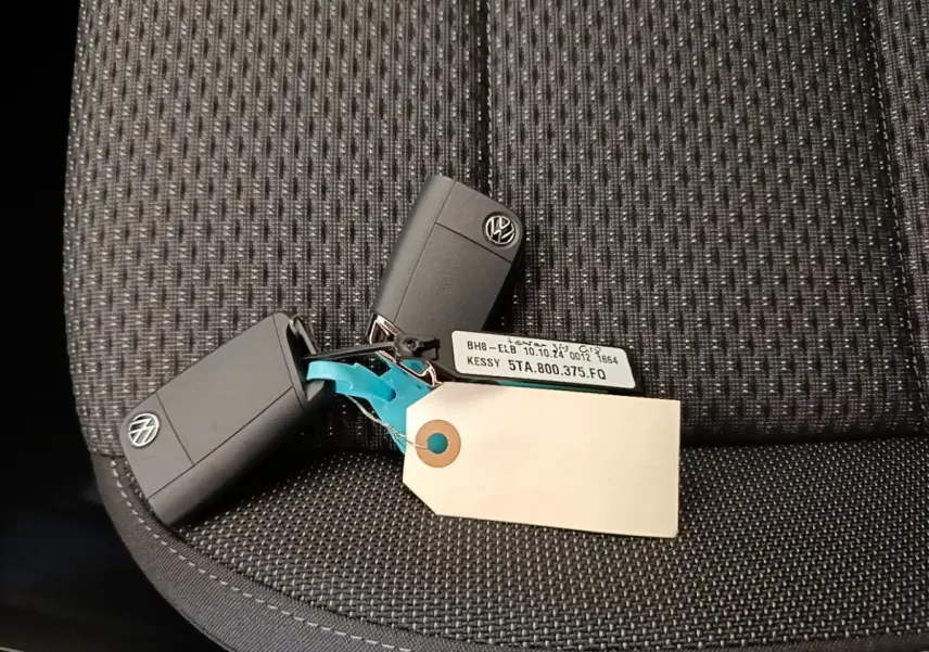 Clés noires Volkswagen posées sur un siège tissu gris foncé, avec une étiquette blanche attachée.
