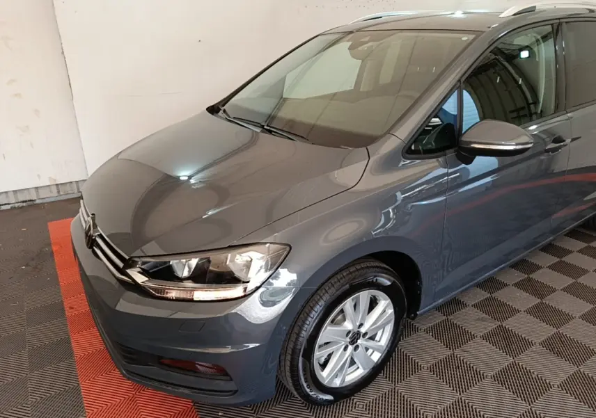 Vue 3/4 avant droit d’un Volkswagen Touran gris clair 2024 avec jantes alliage et feux LED allumés.