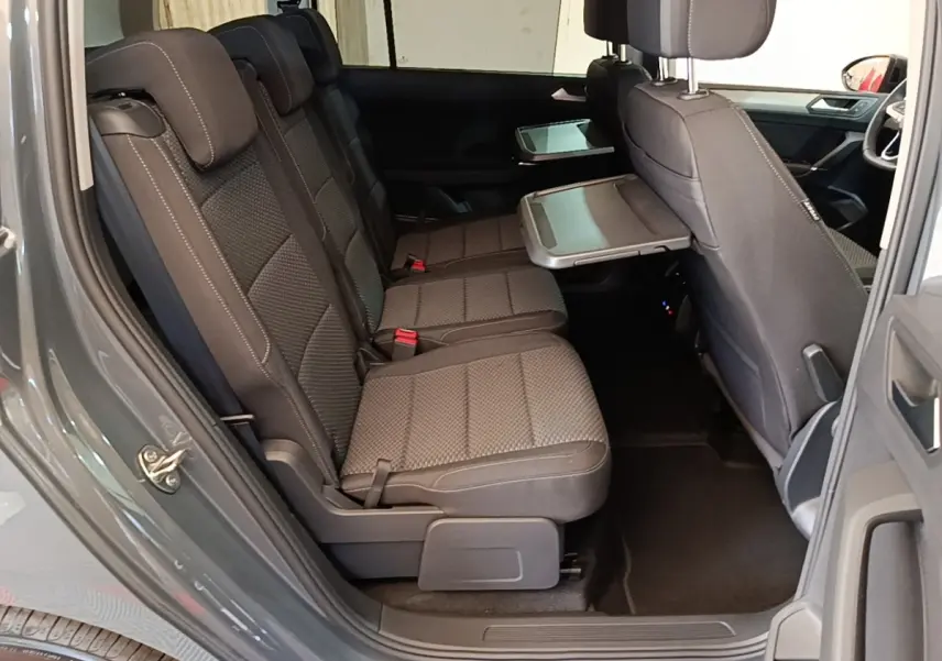 Vue latérale intérieure côté gauche du Volkswagen Touran gris clair 2024, montrant les sièges arrière et une tablette rabattable.