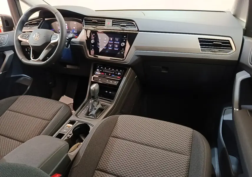 Vue intérieure avant droite du Volkswagen Touran 2024, montrant tableau de bord gris et écran tactile central.