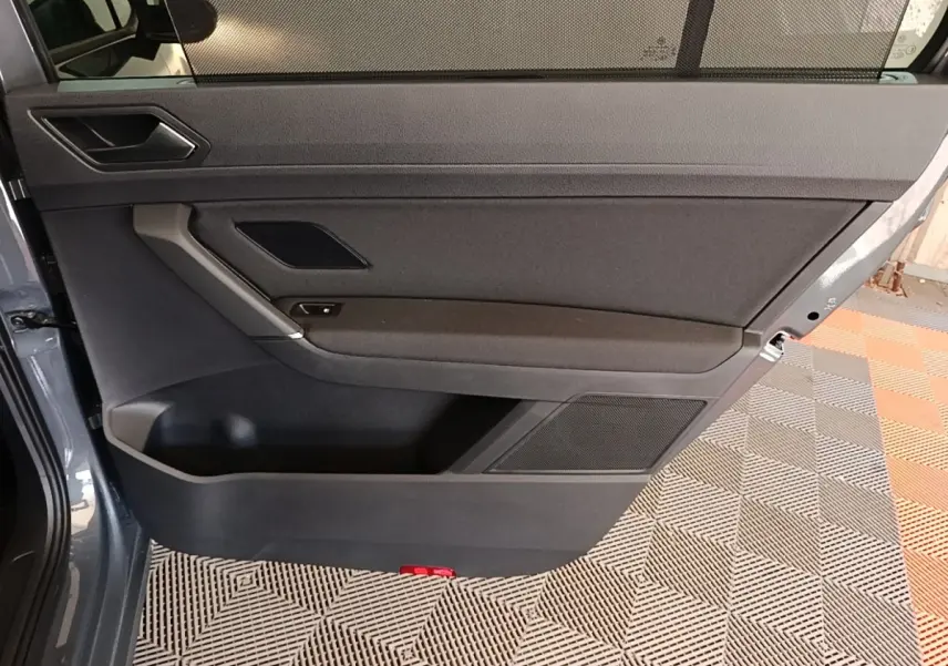 Vue intérieure de la porte avant gauche gris clair du Volkswagen Touran 2024 avec panneau noir et rangement intégré.