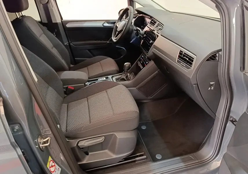 Vue intérieure côté conducteur du Volkswagen Touran gris clair 2024, montrant sièges avant et tableau de bord moderne.