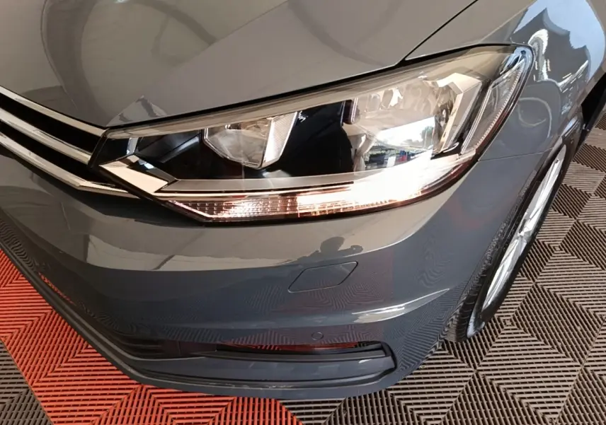 Gros plan sur l'avant droit gris clair du Volkswagen Touran 2024, mettant en valeur le phare LED et la calandre chromée.