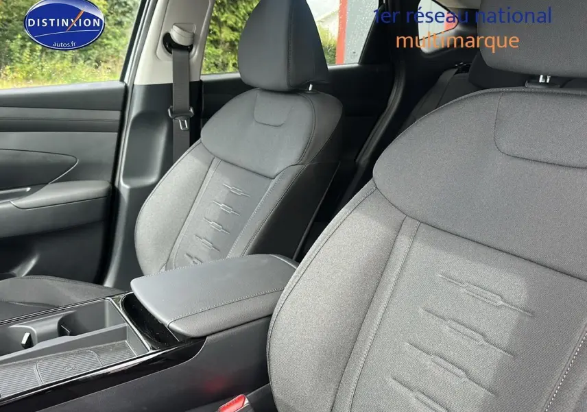 Vue rapprochée des sièges avant gris du Hyundai Tucson 2025 avec accoudoir central et ceinture de sécurité côté gauche.