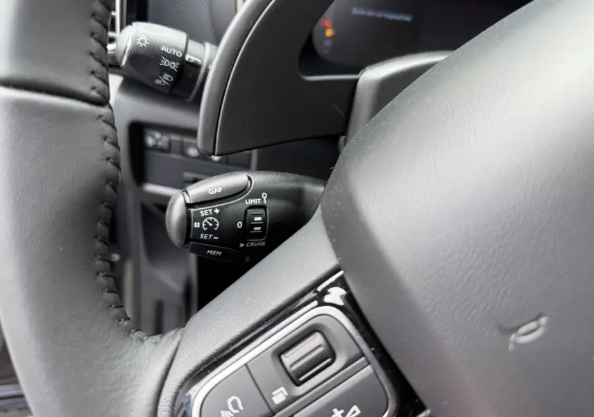 Gros plan sur la commande de régulateur de vitesse à gauche du volant cuir noir du Citroën C5 Aircross 2025.