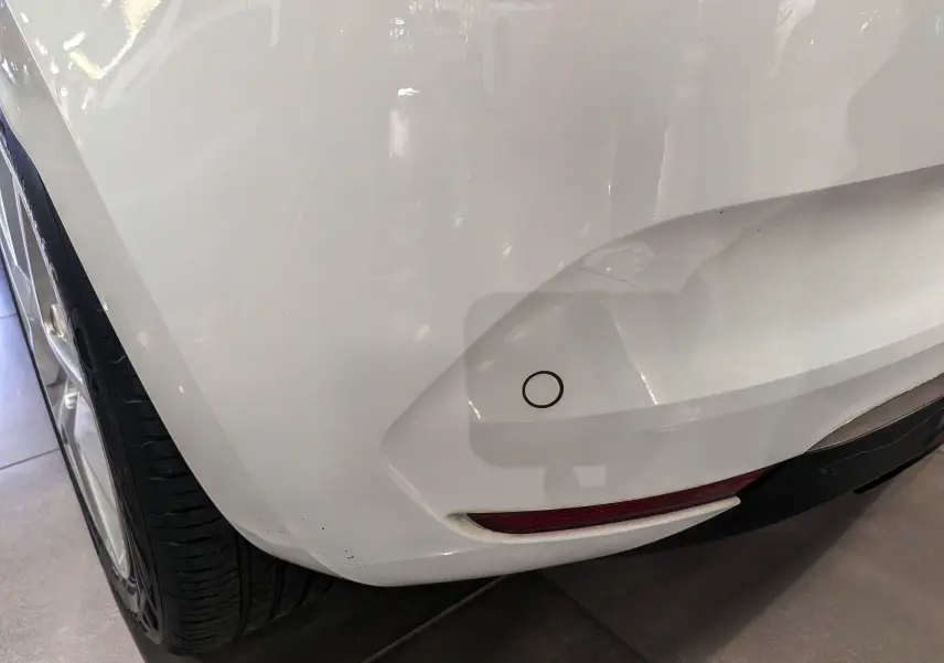 Gros plan sur le pare-chocs arrière droit blanc glacier d'une Renault Clio V TCe 100 CH BUSINESS avec capteur de recul visible.